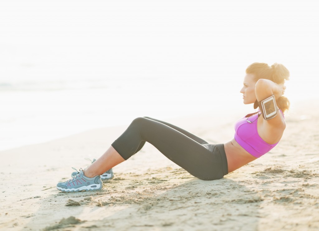 Fitness young woman doing abdominal crunch on beach